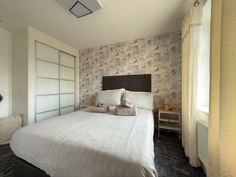 Bedroom with double bed, patterned wallpaper, sliding wardrobe, and window with curtains