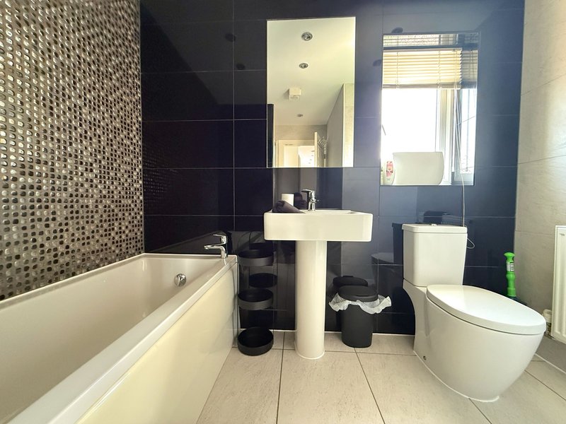 Modern bathroom with bathtub, pedestal sink, toilet, mirror and black tile wall