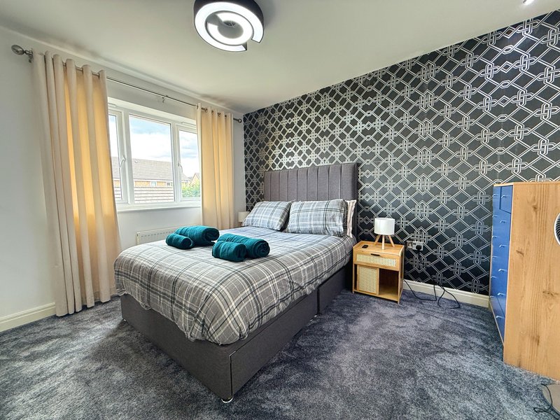 Bedroom with double bed, patterned wallpaper, wooden furniture, and window with yellow curtains