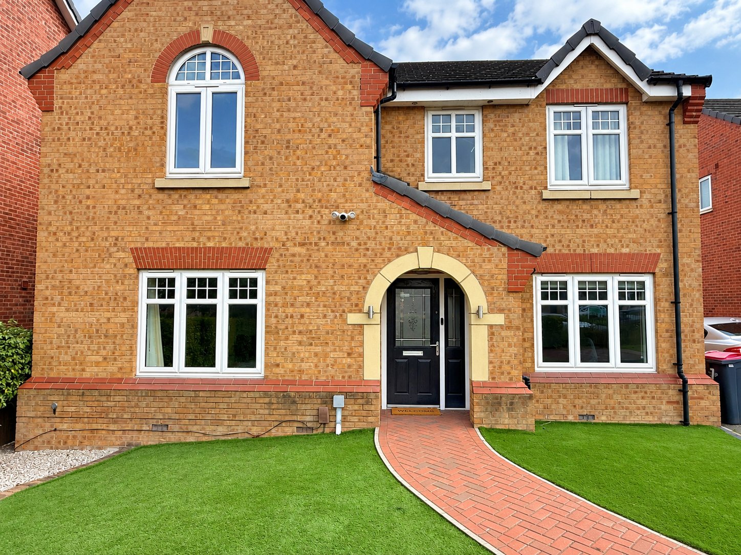 Red brick two-storey detached house with front garden, driveway and manicured lawn