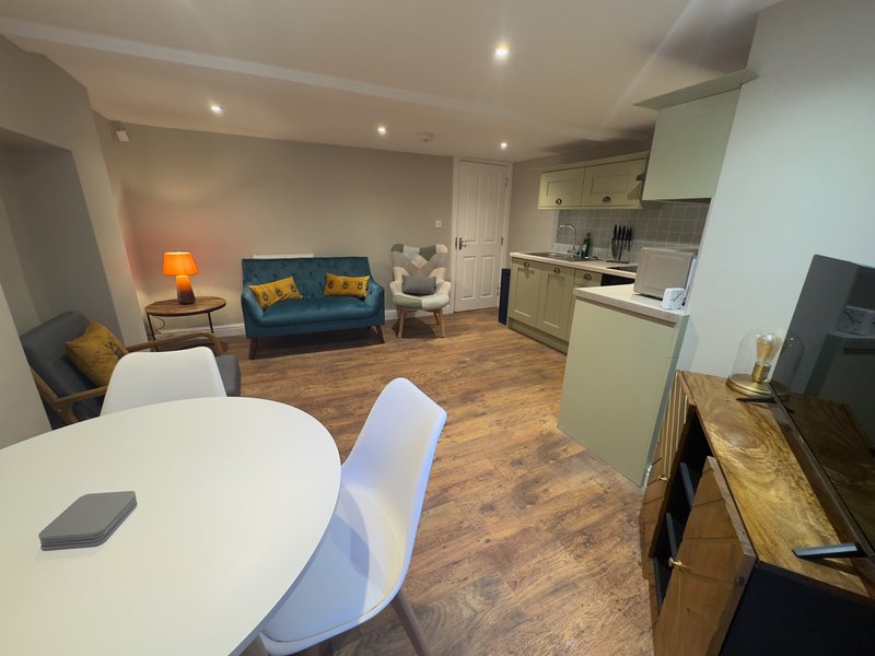 Open-plan living space with dining table, kitchen area, blue sofa and wood flooring
