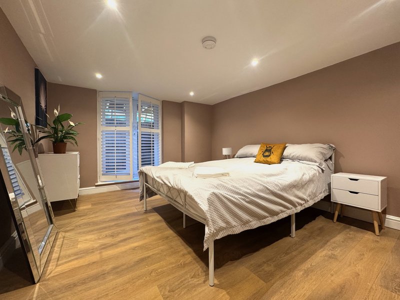 Modern bedroom with double bed, wooden floor, potted plants, and shuttered doors