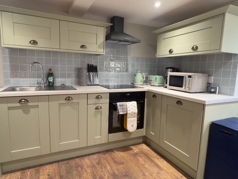 Cream kitchen with grey tile backsplash, black cooker hood, and wooden flooring