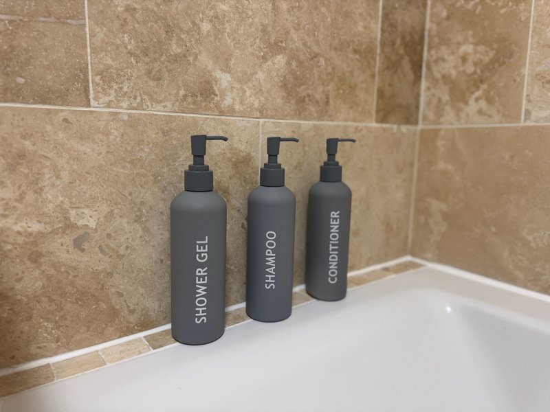 Bathroom counter with three labeled toiletry dispenser bottles and tiled wall