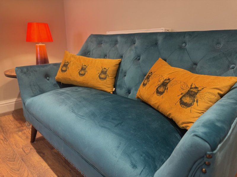 Living room with teal upholstered sofa, yellow patterned cushions, red table lamp, wooden floor