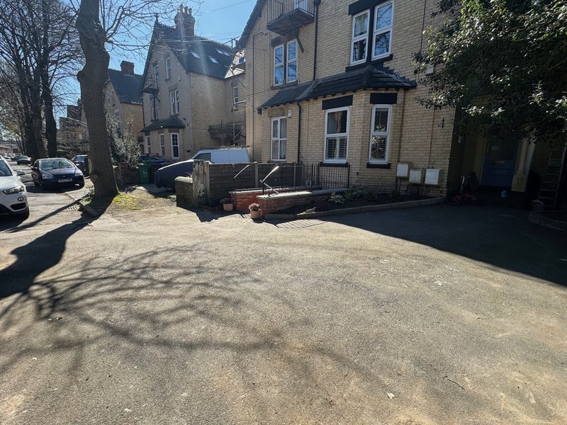 Stone terraced house with driveway, parked cars, and front garden area