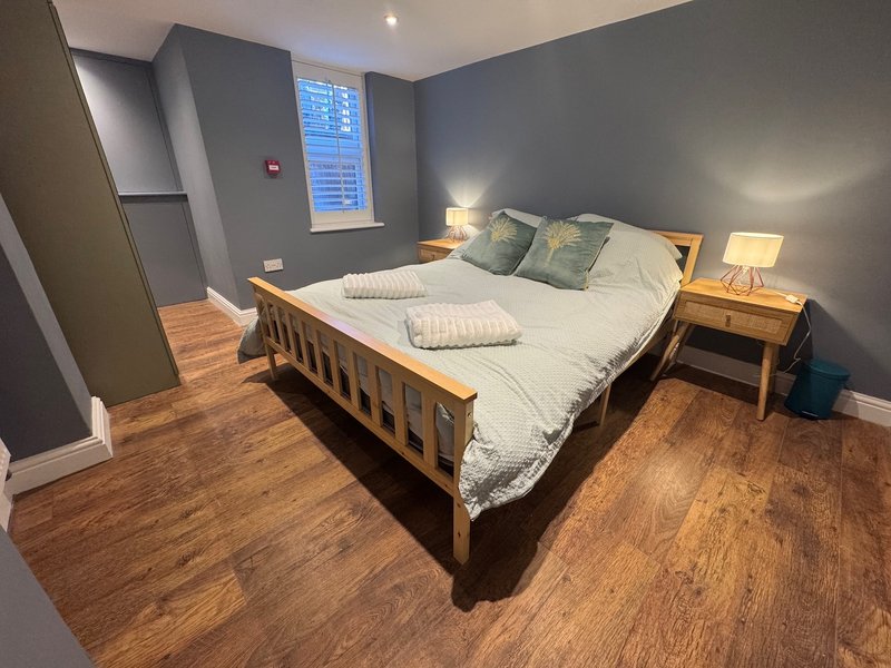 Bedroom with wooden bed frame, white bedding, grey walls, wooden floor and bedside lamp