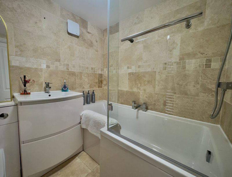 Bathroom with beige tile walls, white vanity, bathtub with glass shower screen