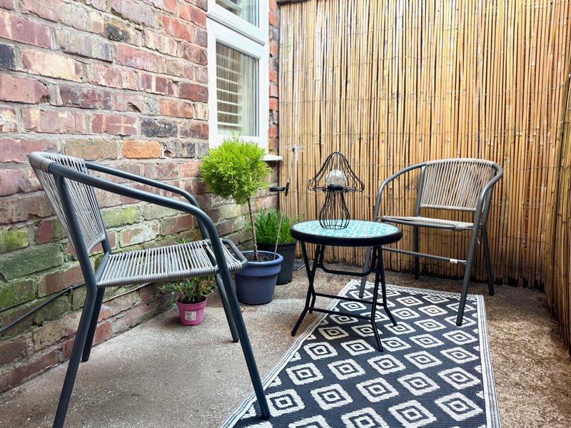 Outdoor patio seating area with black chairs, small table, potted plants and geometric rug