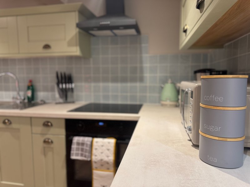 Modern kitchen with white cabinetry, induction hob, grey tile splashback and countertop storage containers