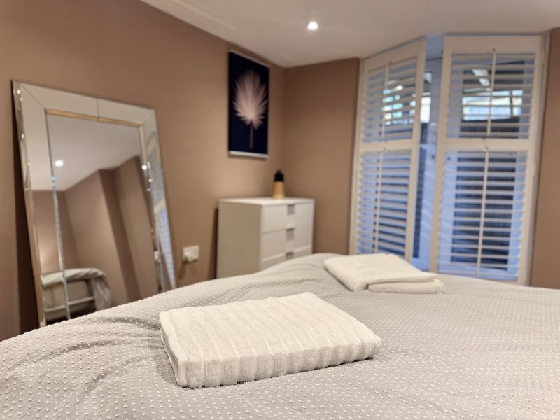 Bedroom with double bed, white pillows, large mirror, white dresser and shuttered windows