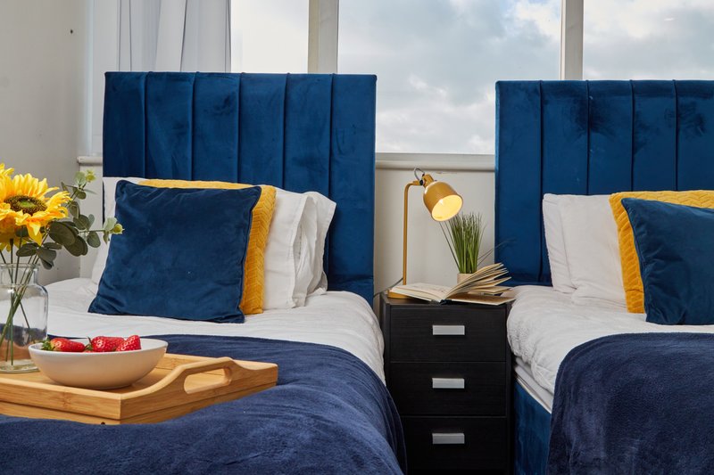 Twin bedroom with blue velvet headboards, white bedding, gold accents and shared nightstand