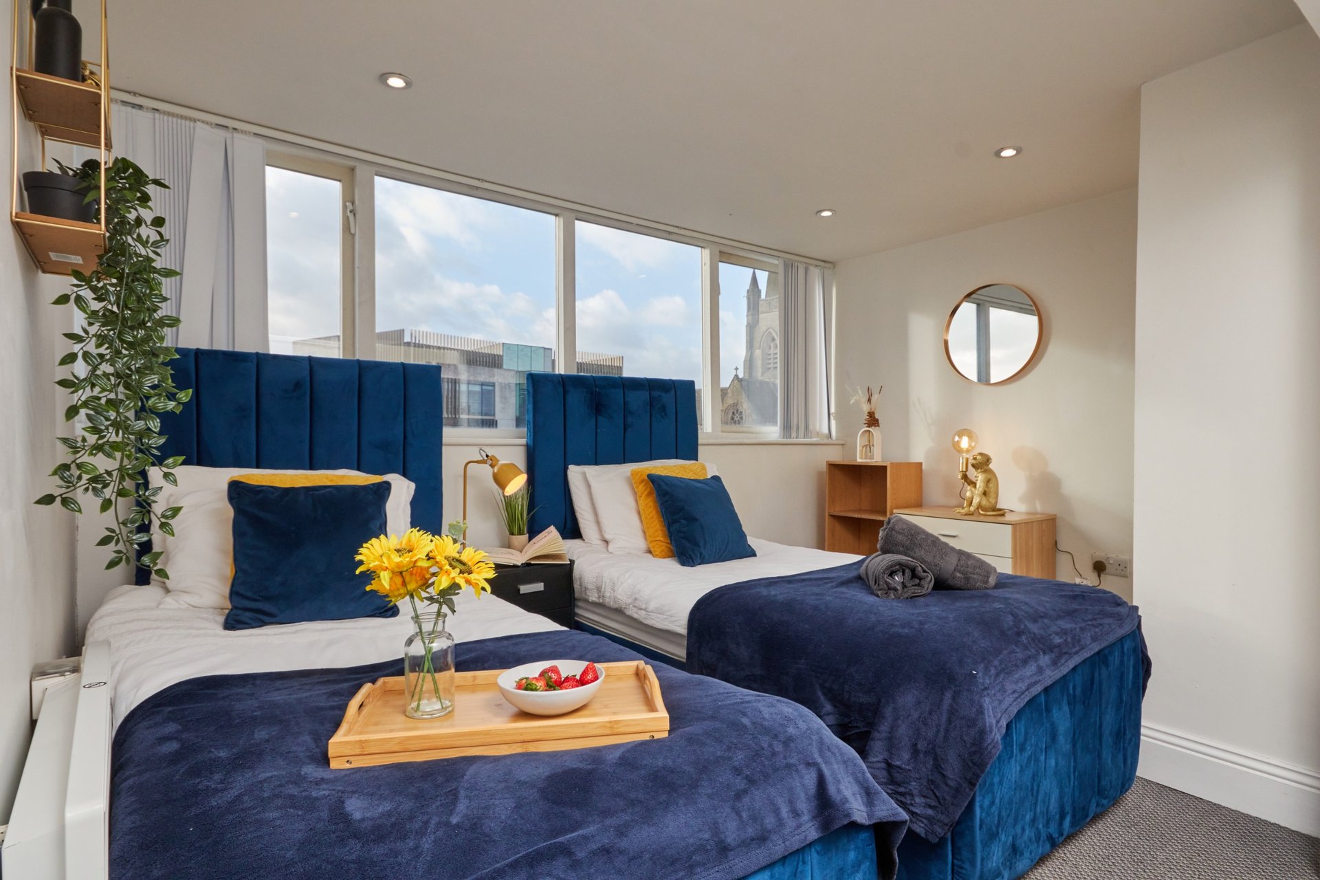 Modern twin bedroom with blue headboards, white bedding, yellow flowers and city view windows