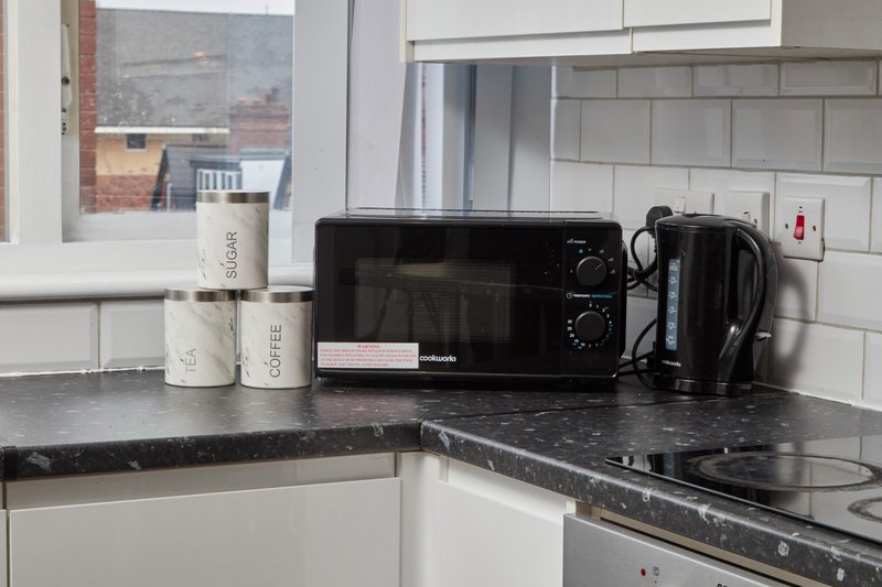 Kitchen corner with black countertop, white subway tiles, microwave, and toiletry containers