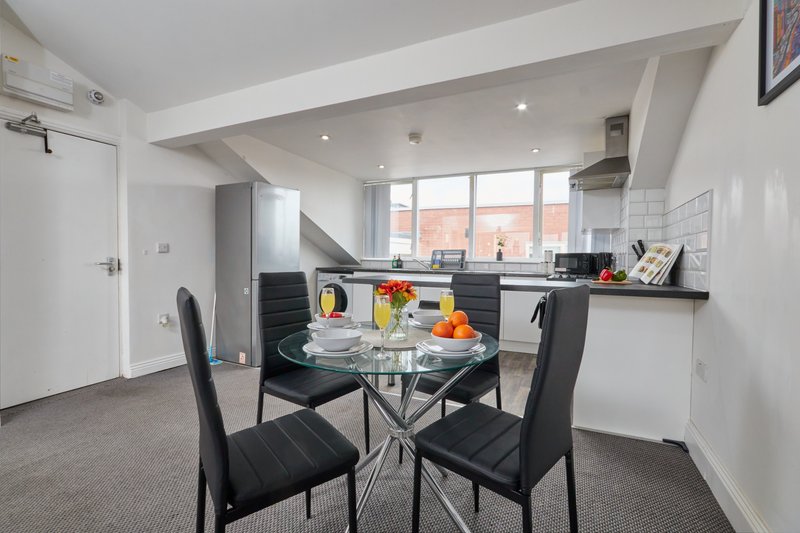 Modern open-plan kitchen and dining area with black chairs, glass table, and city views