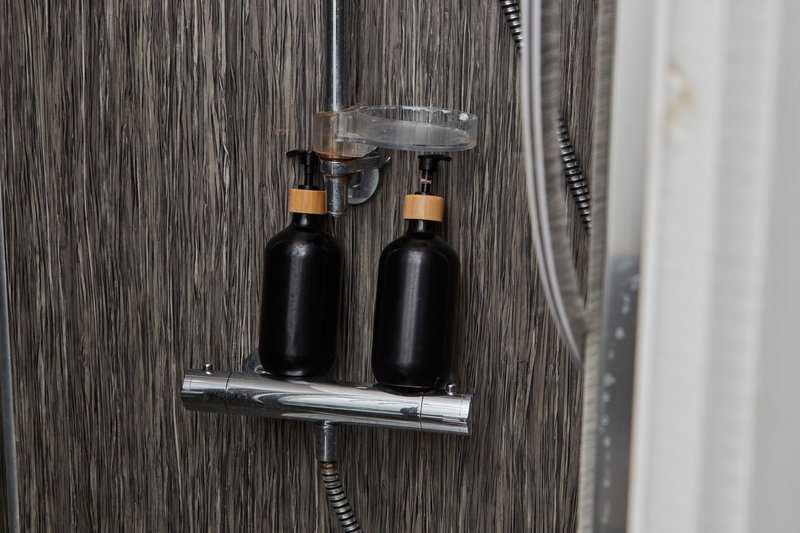 Bathroom shower shelf with two black bottles and chrome fixtures on dark tile wall