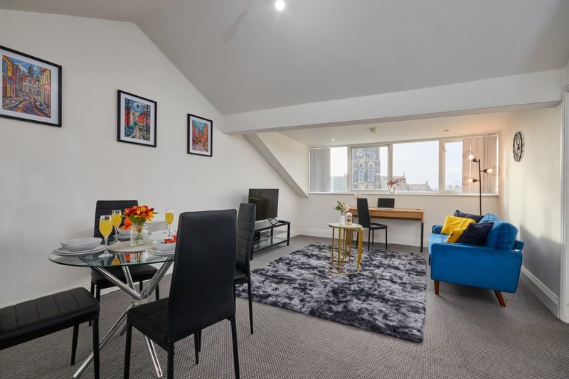 Modern open-plan apartment with dining table, blue armchair, desk area and framed wall art