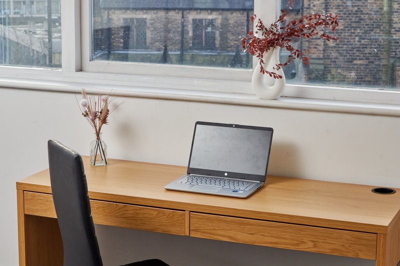 Wooden desk with laptop, chair, and window view of brick buildings