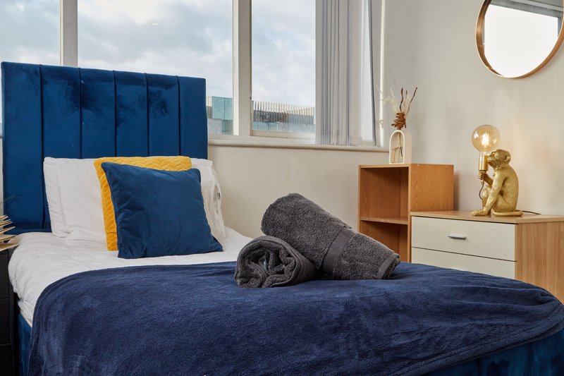 Modern bedroom with blue upholstered headboard, white bedding, and wooden nightstand by large windows