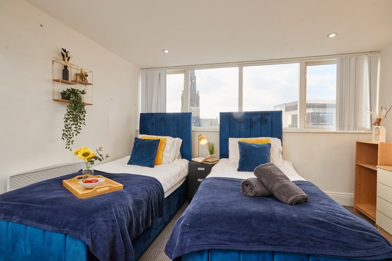 Modern twin bedroom with navy bedding, yellow accents, large windows and city view