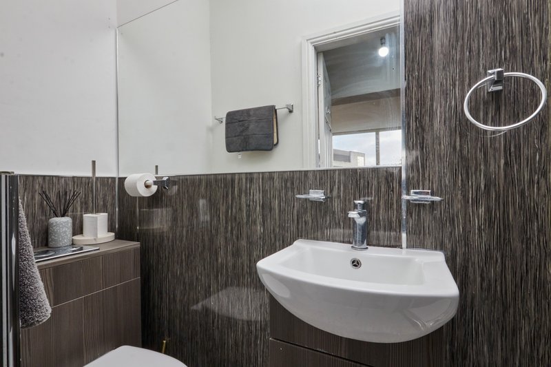 Modern bathroom with curved white sink, dark wood-grain tiles, mirror and toilet