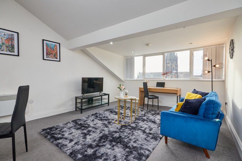 Modern open-plan living room with blue sofa, desk, TV stand, and large windows