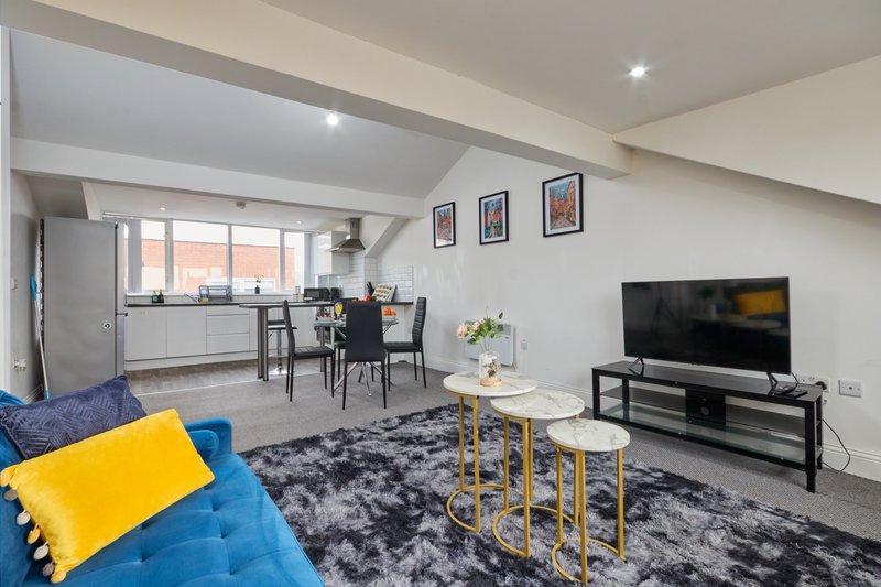 Modern open-plan living area with blue sofa, TV, dining table and kitchen area