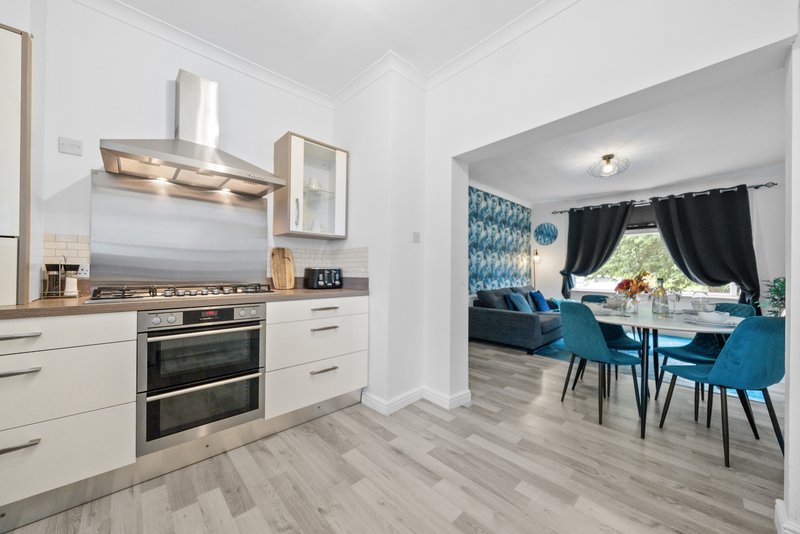 Modern kitchen with white cabinetry, stainless steel appliances and wooden flooring, adjoining dining area