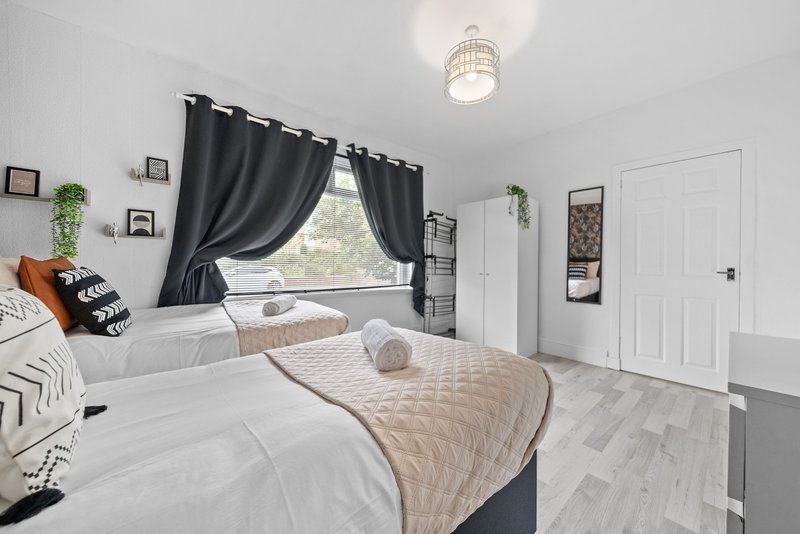Bright bedroom with two beds, black curtains, window view, and white wooden flooring
