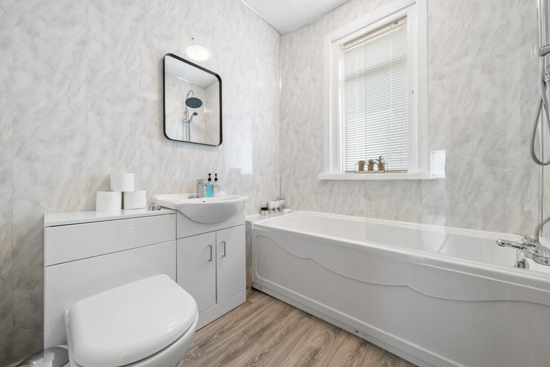 Modern bathroom with white toilet, sink vanity, bathtub and marble-effect wall tiles