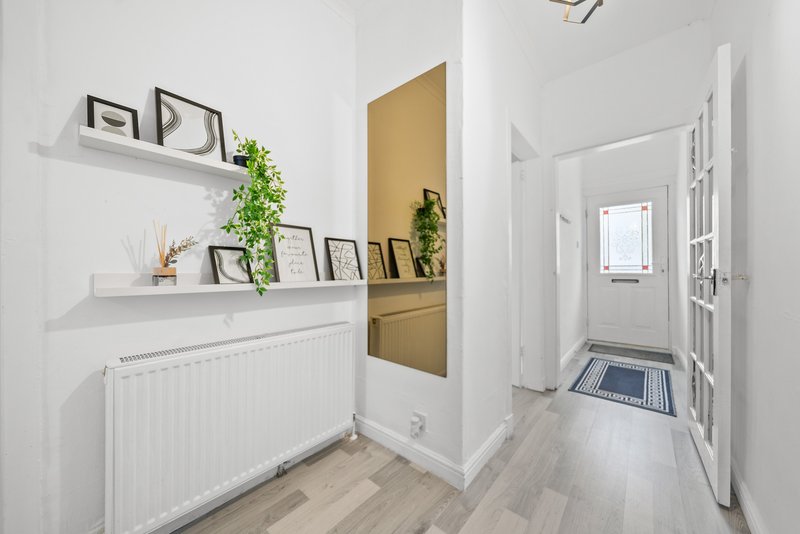 Modern hallway with white walls, floating shelves, radiator, plants and framed artwork