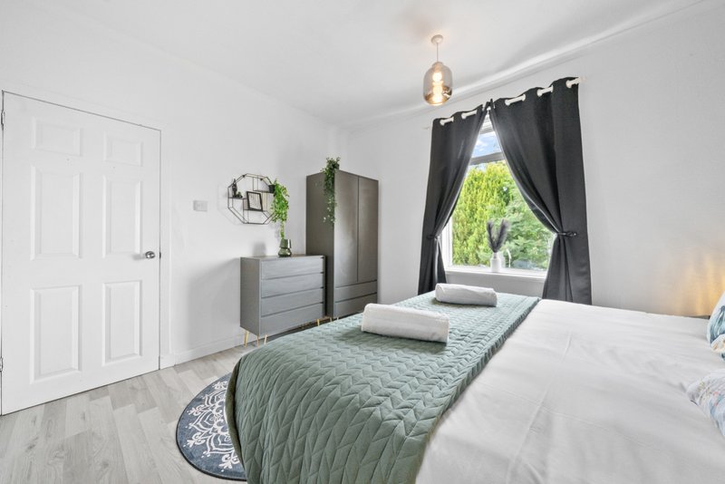 Bright bedroom with two single beds, grey bedding, wooden dresser, and black curtains framing window