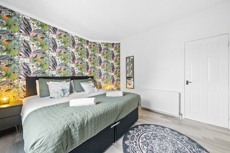 Bedroom with double bed, patterned wallpaper, bedside lamps, white door and wooden flooring