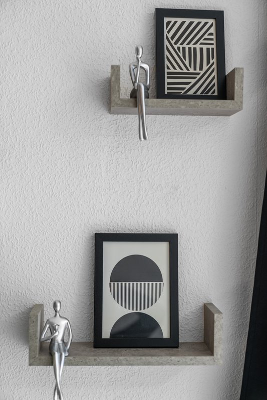 White wall with two floating shelves displaying framed black and white geometric artwork and decorative objects