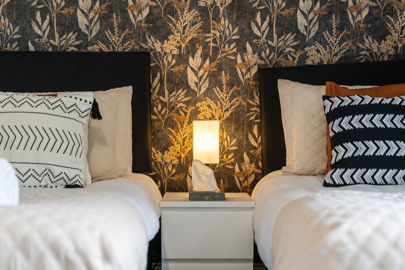 Twin bedroom with patterned wallpaper, decorative pillows, bedside lamp and white bedding
