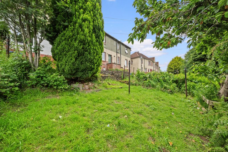 Rear garden view with lawn, stone property, mature trees and hedges