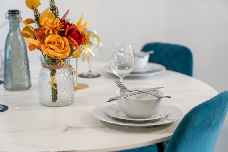 Dining table set with white plates, glasses, cutlery and yellow flower arrangement
