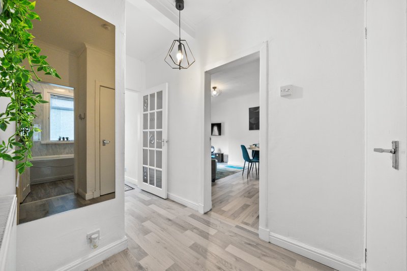Modern hallway with light wood flooring, white walls, pendant light fixture, and open doorways