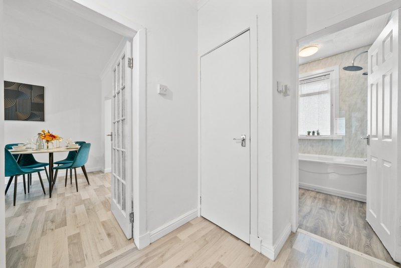Modern hallway with white doors, wooden flooring, and glimpse of dining area with turquoise chairs