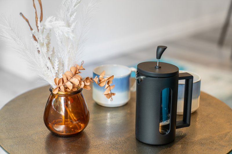 Wooden table with decorative vase, dried flowers, ceramic mug, and black coffee maker