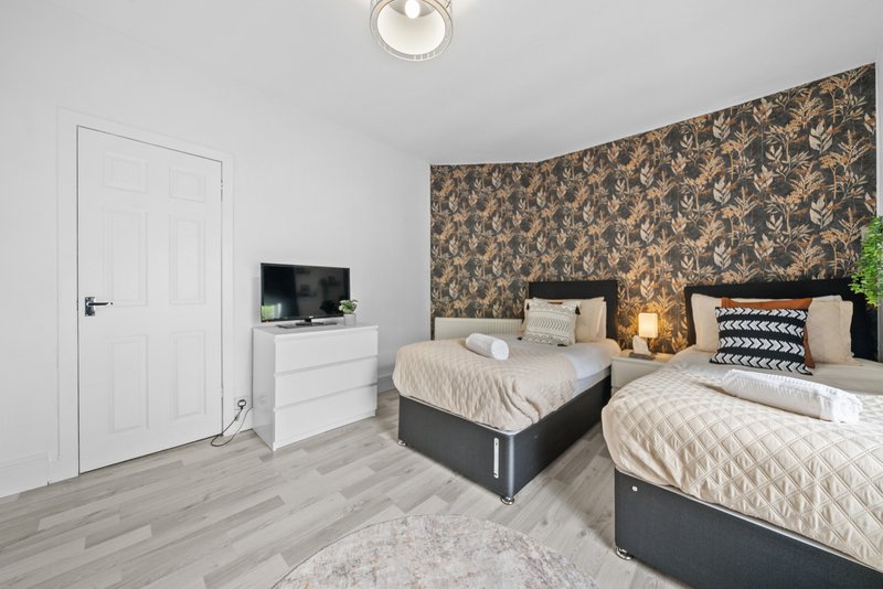 Modern bedroom with two beds, patterned accent wall, TV on dresser and white door