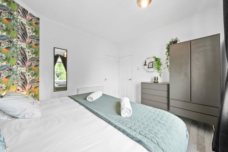 Bright bedroom with two beds, gray wardrobe, botanical wallpaper, and potted plants