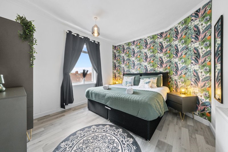 Modern bedroom with double bed, patterned wallpaper, dark curtains and wooden flooring