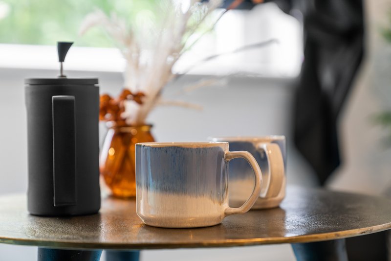 Round table with black coffee press, glass mugs, and dried flowers in vase