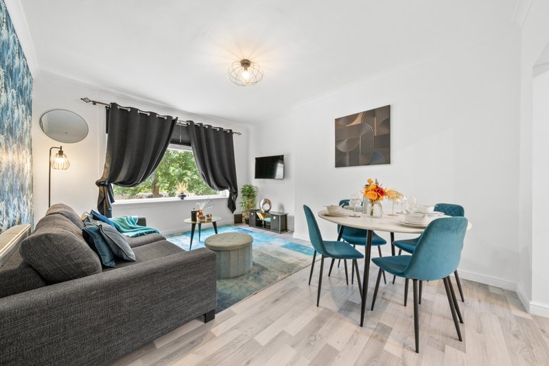 Open-plan living and dining area with gray sofa, teal dining chairs, wooden table, and large window