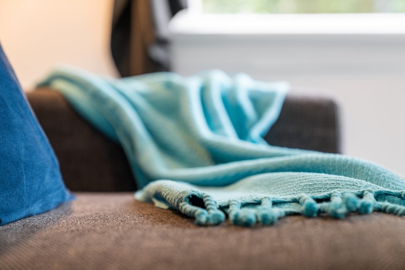 Close-up of turquoise striped throw blanket and beaded accessory on brown sofa