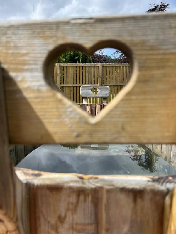 Wooden hot tub with heart-shaped window cutout framing garden view