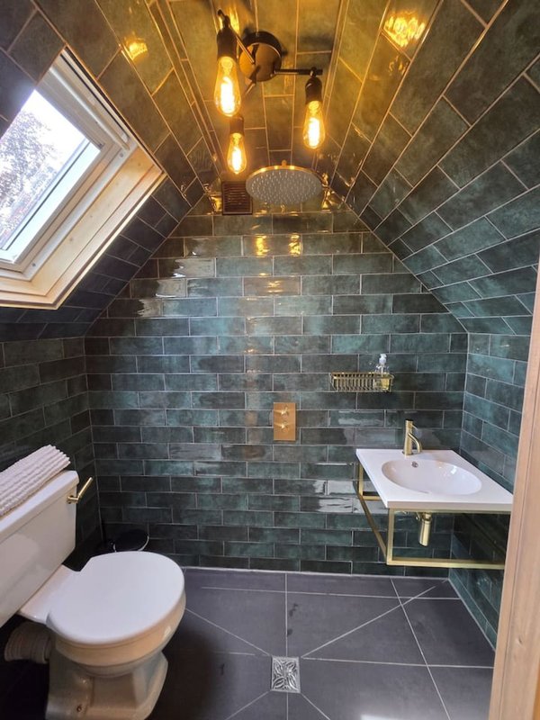 Modern bathroom with dark tiled walls, white toilet, pedestal sink, and pendant lighting