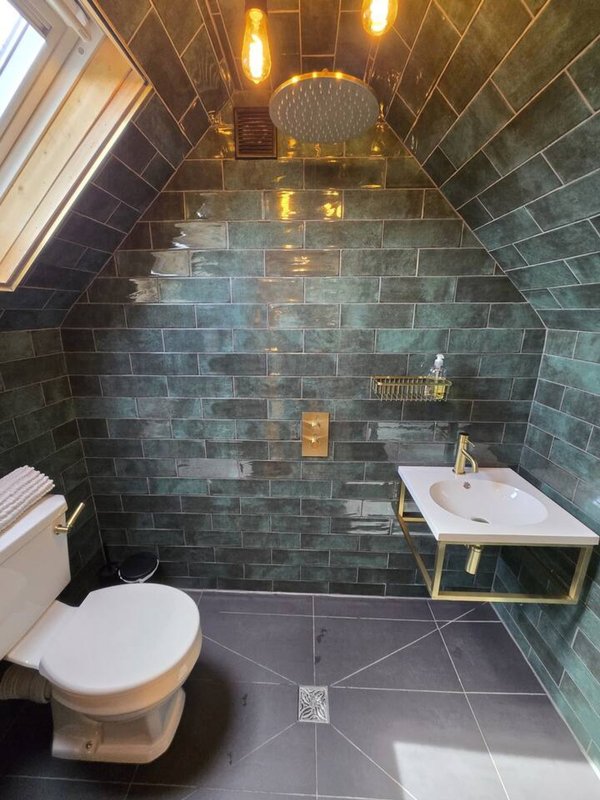 Modern bathroom with dark tile walls, walk-in shower, toilet, and white sink on brass frame