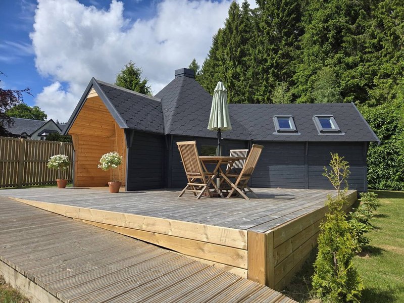 Modern black and wood exterior building with wooden deck, seating area and garden surroundings